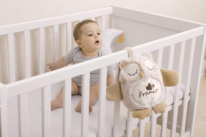 Beżowa pluszowa sowa z imieniem przymocowana do łóżeczka